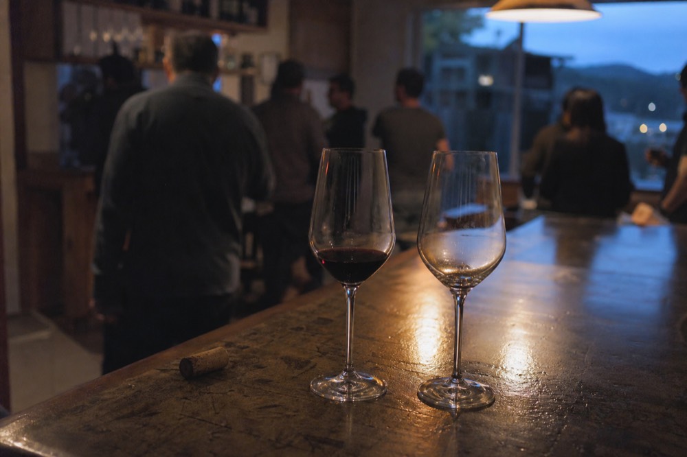 Wine glasses on a wooden tasting bar in a dim tasting room, no text, no logos, no people