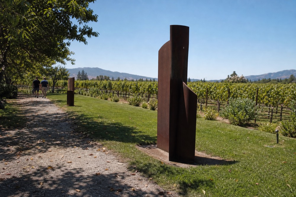 Sculptures set among vineyard rows on an estate lawn, no text, no logos, no people