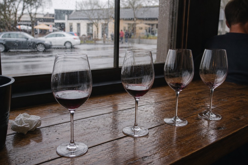 A flight of red wines on a wooden tasting room bar, no text, no logos, no people