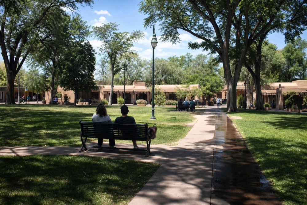 Historic town plaza with green lawns and trees surrounded by low buildings, no text, no logos, no people