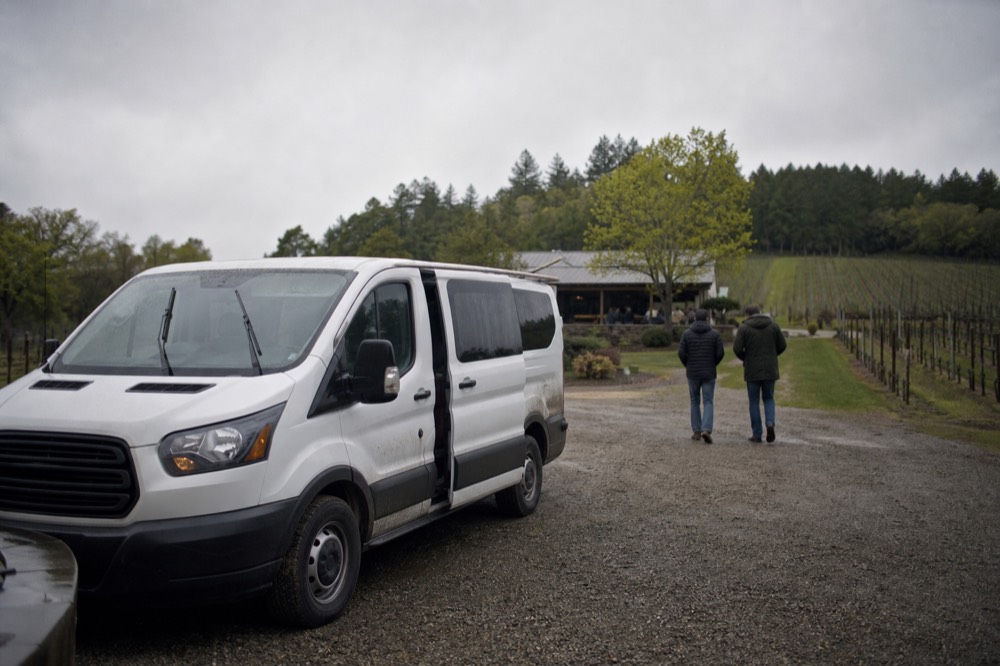 A wine tour van parked in front of a vineyard with tasting room, no text, no logos, no people