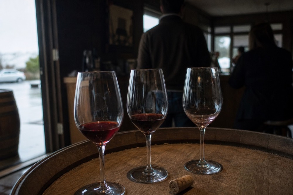 Three wine glasses on a barrel top in a dim Sonoma tasting room, no text, no logos, no people.