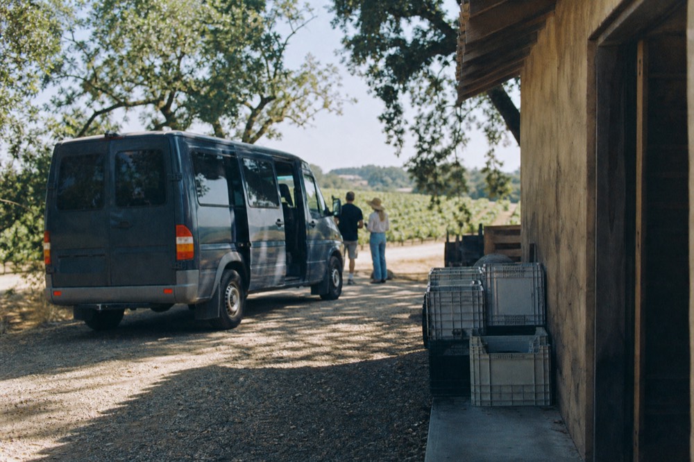 A small tour van parked beside a winery driveway in Sonoma County, no text, no logos, no people